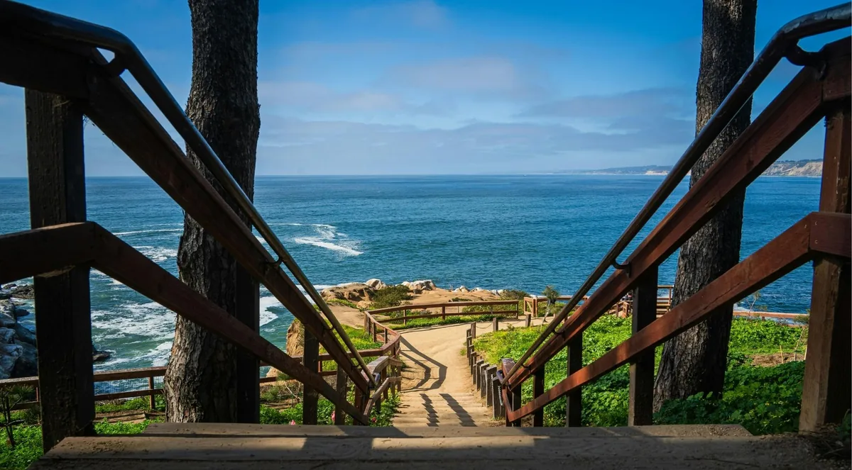 Wooden staircase and railings leading down to a fenced clifftop overlook above the ocean