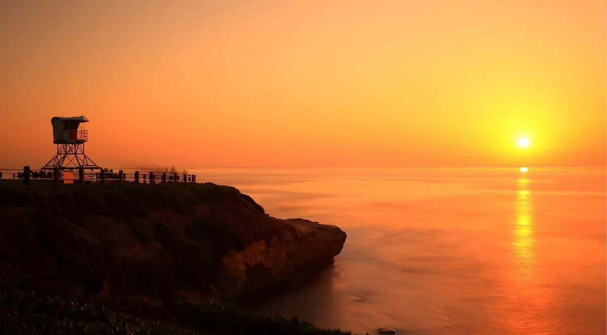 A lifeguard tower silhouetted on the bluff above the ocean as the sun touches the horizon